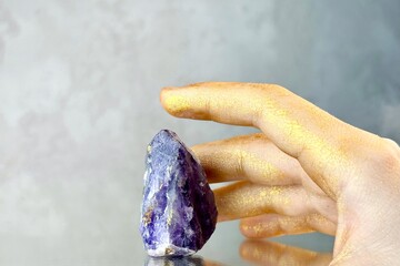 
Close-up hand trying to touch amethyst crystal on grey abstract background. Mystical atmosphere in...