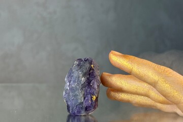 
Close-up hand trying to touch amethyst crystal on grey abstract background. Mystical atmosphere in...