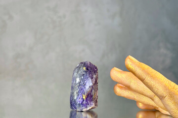 
Close-up hand trying to touch amethyst crystal on grey abstract background. Mystical atmosphere in...
