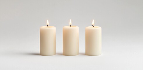 Soft light and hazy shadows isolate three white wax candles positioned on a table, creating a warm and subtle lighting effect