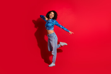 Young cheerful woman posing energetically on vibrant red background, showcasing trendy outfit with...