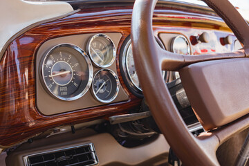 Dashboard of a classic car with wood accents, chrome analog dials and a brown leather steering...
