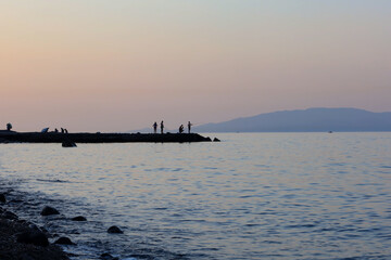 Obraz premium Silhouettes of people fishing on a rocky pier