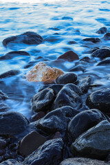 a group of smooth, dark rocks scattered along the shore, partially submerged by water. A...