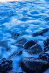 ocean waves washing over smooth black volcanic rocks on a coastal shoreline, captured with long exposure for a soft, ethereal effect