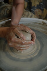 Women's hands shaping gray clay on a potter's wheel.