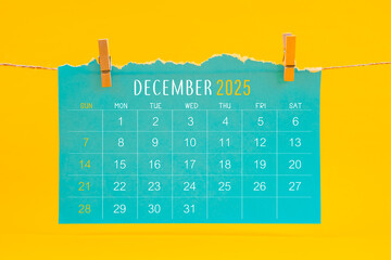 December 2025 calendar tearing hanged with brown rope on yellow background.