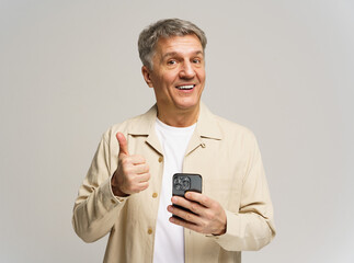 Man smiles and gives a thumbs up while holding a smartphone against a light background