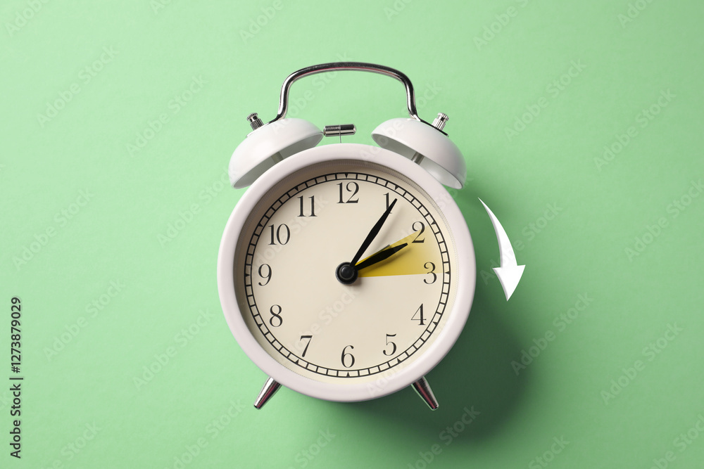 Poster Daylight saving time. White alarm clock on light green background, top view. Highlighted area and arrow showing time change by one hour forward