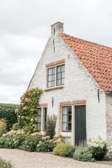 Obraz premium A delightful white cottage featuring a striking red roof sits surrounded by a lush and vibrant garden, all within a peaceful countryside setting on a cloudy day