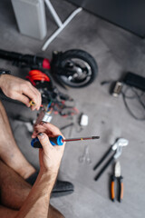 man tries to fix an electric scooter with his own hands at home. Electricity and the danger of getting an electric shock.