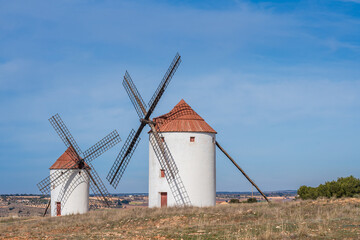 Two white-washed, traditional Spanish windmills with wooden blades stand tall in Mota del Cuervo, La Mancha, Spain