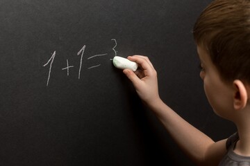 Child solving a math problem on a blackboard, erasing an answer. Ideal for themes of education,...
