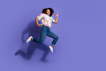 Joyful young woman with curly hair jumps energetically against a vibrant purple background