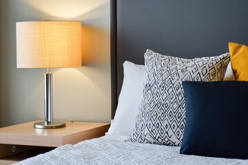 Cozy bedroom interior with bedside lamp illuminating decorative pillows on a comfortable bed in a modern hotel room for relaxation and sleep