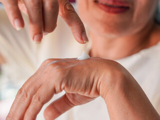 Lifestyle Health Care. Asian senior woman applying lotion to her hands and arms in her living room at home during the holidays. Skin care with moisturizers and natural extracts. Elderly health