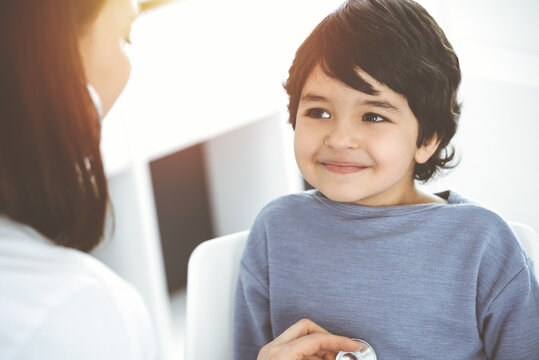Doctor-woman examining a child patient by stethoscope in sunny clinik. Medicine concept