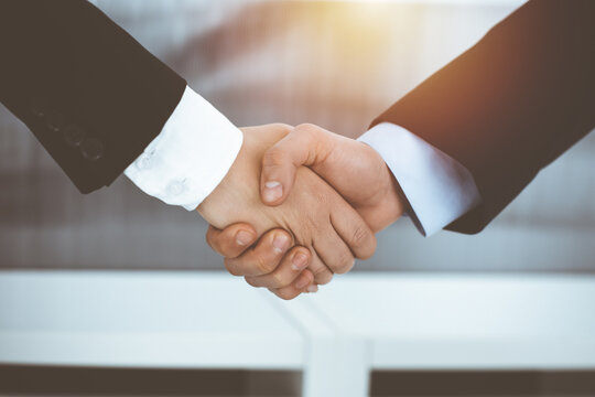 Businessman and woman shaking hands in sunny office, close-up. Concept of handshake as success symbol in business