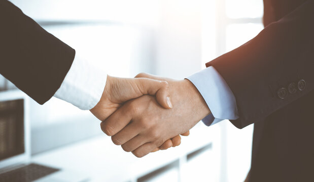 Businessman and woman shaking hands in sunny office, close-up. Concept of handshake as success symbol in business