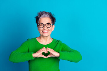 Smiling elderly woman making a heart with hands against a vibrant blue background