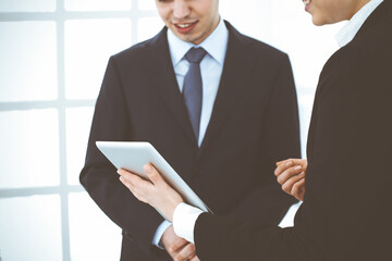 Businessman and woman using tablet computer for discussing questions in office. Partners or colleagues at meeting. Business cooperation concept