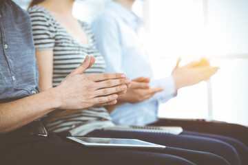 Business people clapping at meeting or conference, close-up of hands. Group of unknown businessmen and women in sunny office