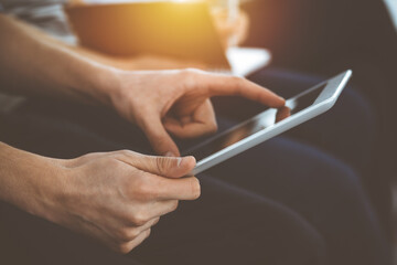 Group of casual dressed business people working at meeting or conference in sunny office, close-up of hands. Businessman using tablet computer