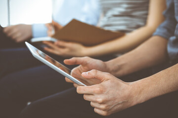 Group of casual dressed business people working at meeting or conference, close-up of hands. Businessman using tablet computer. Teamwork or coaching concept