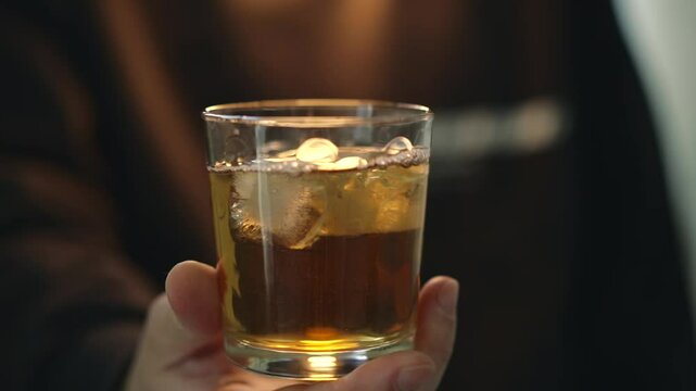 Glass of whiskey close-up.
Alcohol addiction.
A man drinks a talkgol drink with ice at a bar.
A man holds a glass of whiskey.
Whiskey with ice in a glass glass