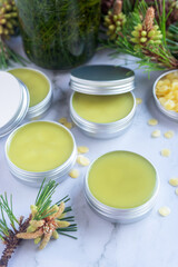 homemade pine needles salve balm in reusable aluminum box on white marble background.
