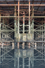 Detailed view of a corroded, timeworn pier understructure with rusted beams, weathered concrete, and marine growth, forming a striking architectural pattern reflected in calm water