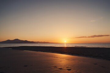 Fototapeta premium arafed view of a beach with a sunset and a person walking on the sand