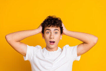 Surprised young man with curly hair in casual white shirt holding his head, colorful orange background