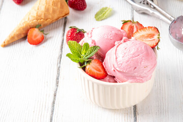 Summer refreshing cold dessert, tasty and aromatic strawberry ice cream, homemade berry sorbet in ceramic bowl, with fresh strawberries, ice cream waffle cones on white wooden background