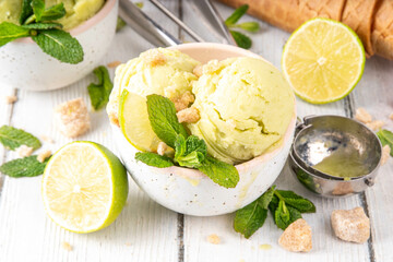Summer refreshing cold dessert, tasty aromatic mojito or key lime pie ice cream, homemade sorbet with mojito cocktail flavor in ceramic bowl, with fresh lime, mint, waffle cones on wooden background