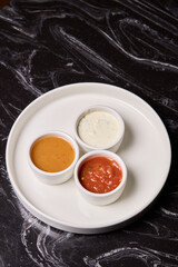 A decorative plate holds three enticing dipping sauces, each unique in flavor and color