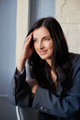 woman in a stylish gray suit poses in a modern office setting with soft lighting. Her long black...