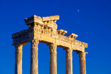 Temple of Apollo at sunset  with a crescent moon in the sky above it. The temple was built in the 2nd century AD during the Roman Empire. Side, Manavgat, Antalya province, Turkey