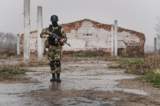 special forces soldier with an automatic rifle wearing a helmet mask and body armor with a drone stands against the background of destroyed buildings. The concept of the army and military exercises.