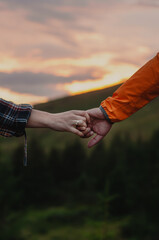 two hands holding each other on the background of sunset and mountains, hand in hand,...