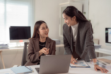 Two professional women engaging in a productive discussion at a desk, surrounded by laptops and documents, highlighting teamwork and collaboration in a contemporary office environment