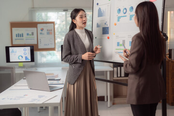 Two business professionals engage in a discussion about data analysis in a modern office setting. Charts and graphs on a board and screens highlight the focus on financial growth and planning