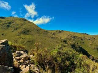 Green hills covered with grasslands, a rocky trail, blue sky with clouds and a valley in the distance