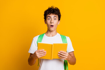 Young male student in a casual white t-shirt reading a book on a vibrant yellow background with a...