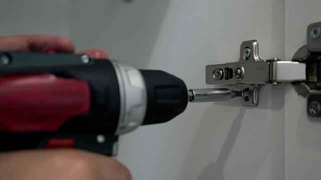 A man uses a screwdriver to fasten hinges for cabinet doors