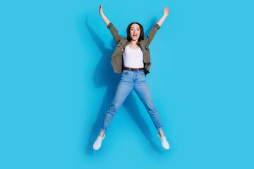 Joyful young woman jumping against a vibrant blue background in casual outfit and expressing happiness