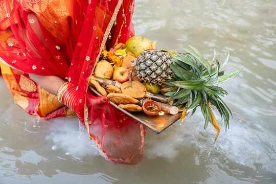 Woman offering fruits and sweets during chhath puja in river water