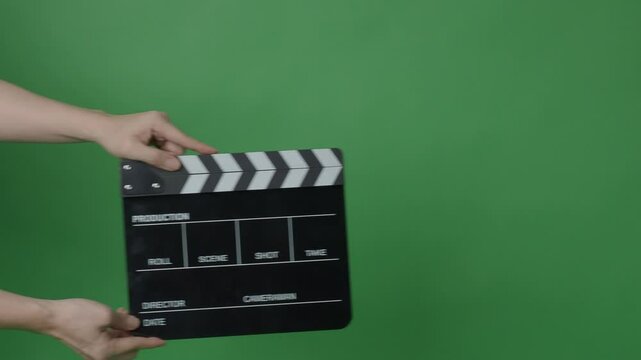A classic black and white film clapperboard or movie slate being held in front of a green screen. Essential filmmaking tool is used to mark scenes and synchronize audio and video in film production.