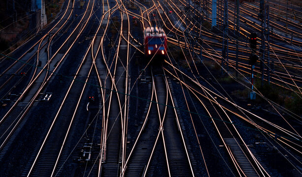 A single electric locomotive makes its way through the complicated track network of a freight yard in Hagen (NRW, Germany) in the twilight of the rising sun. Railroad panorama with glistening tracks.