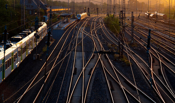 Morning atmosphere above the tracks of the goods station in Hagen-Vorhalle shortly after sunrise. Local trains meet on the platform. Countless sidings and shunting tracks glisten in the warm light